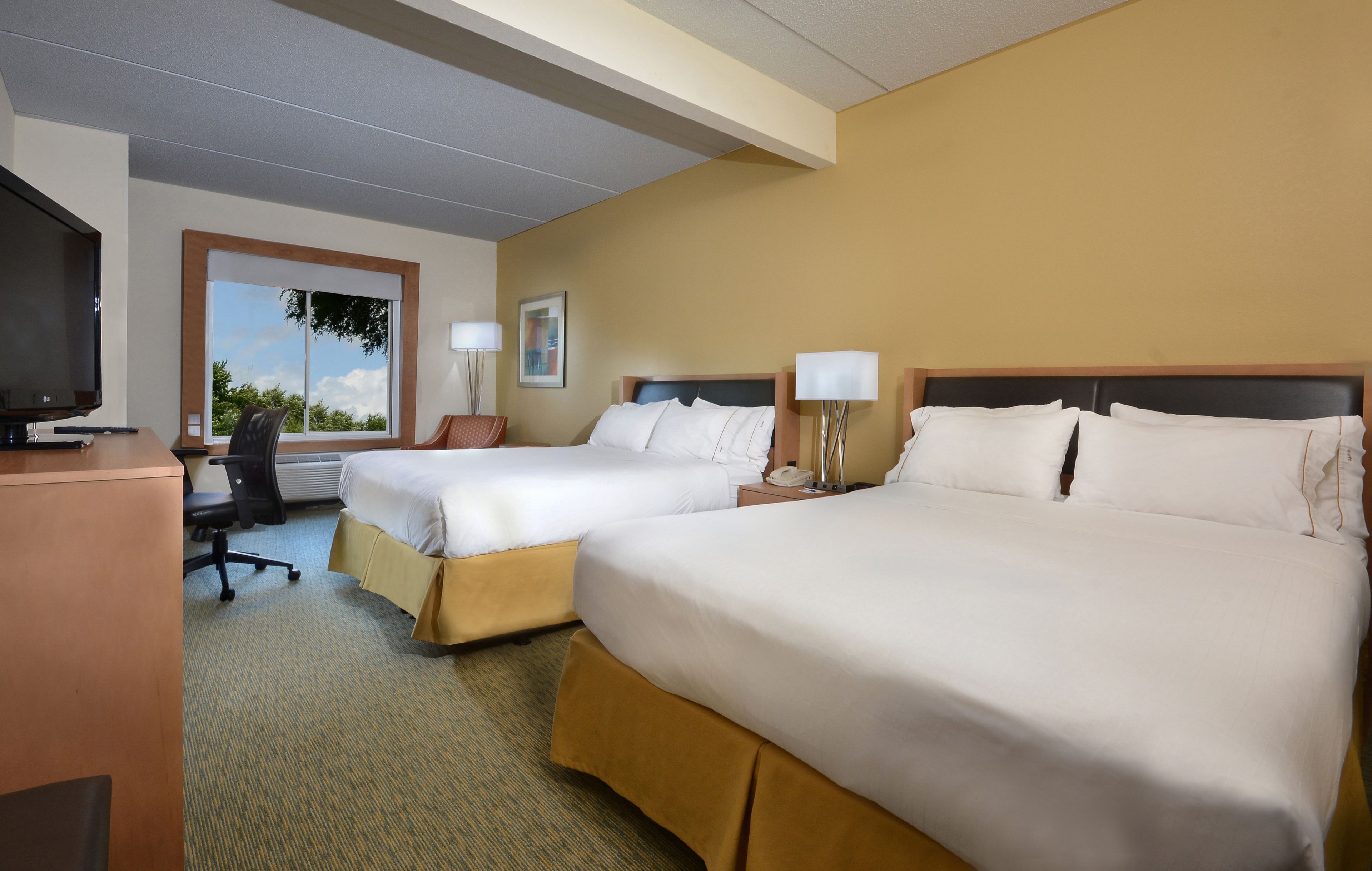 A hotel room with two beds, a desk, a TV, and a window with a view.