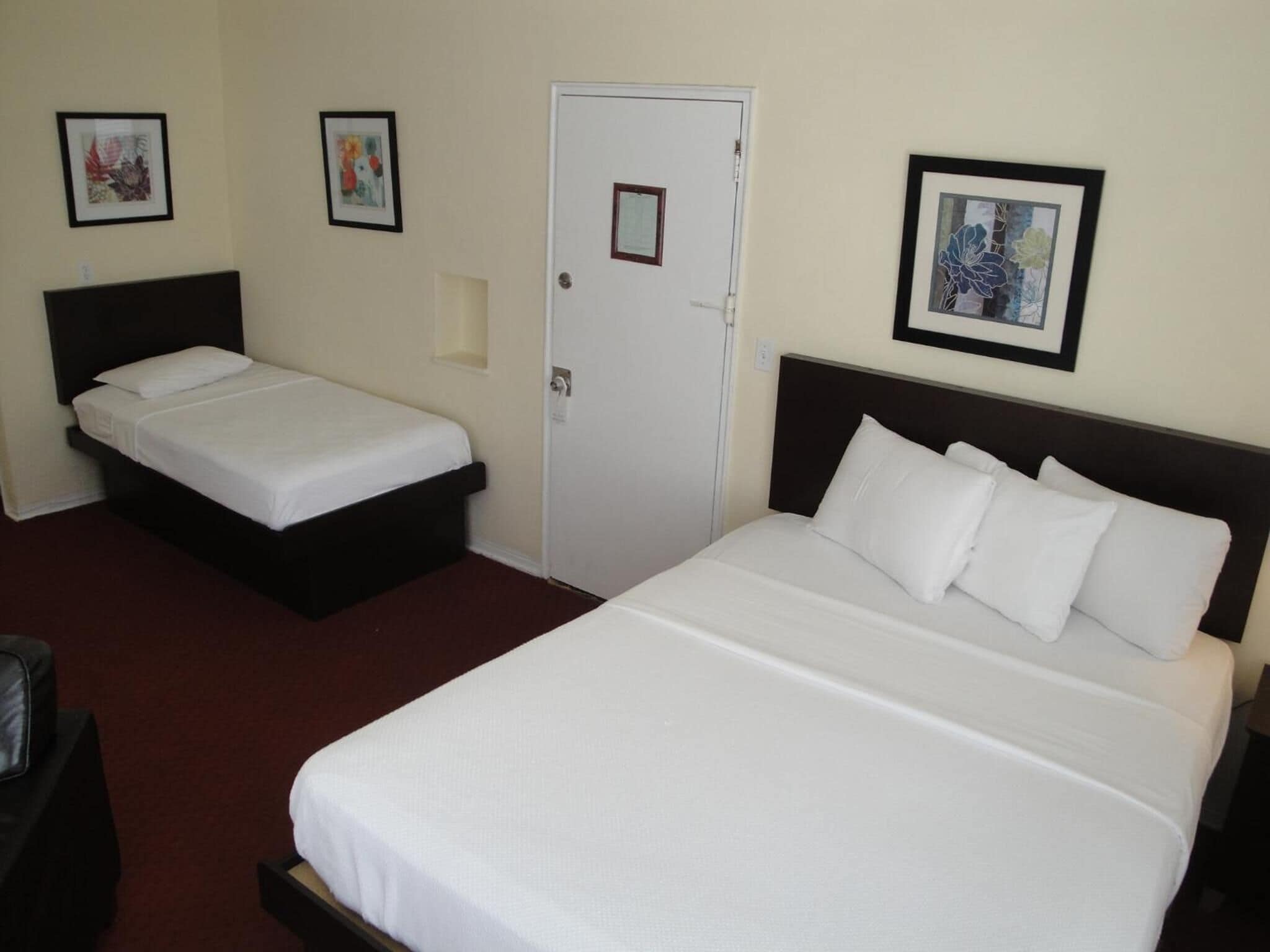 A hotel room with two single beds and a larger bed, each with white bedding. There are framed pictures on the walls.