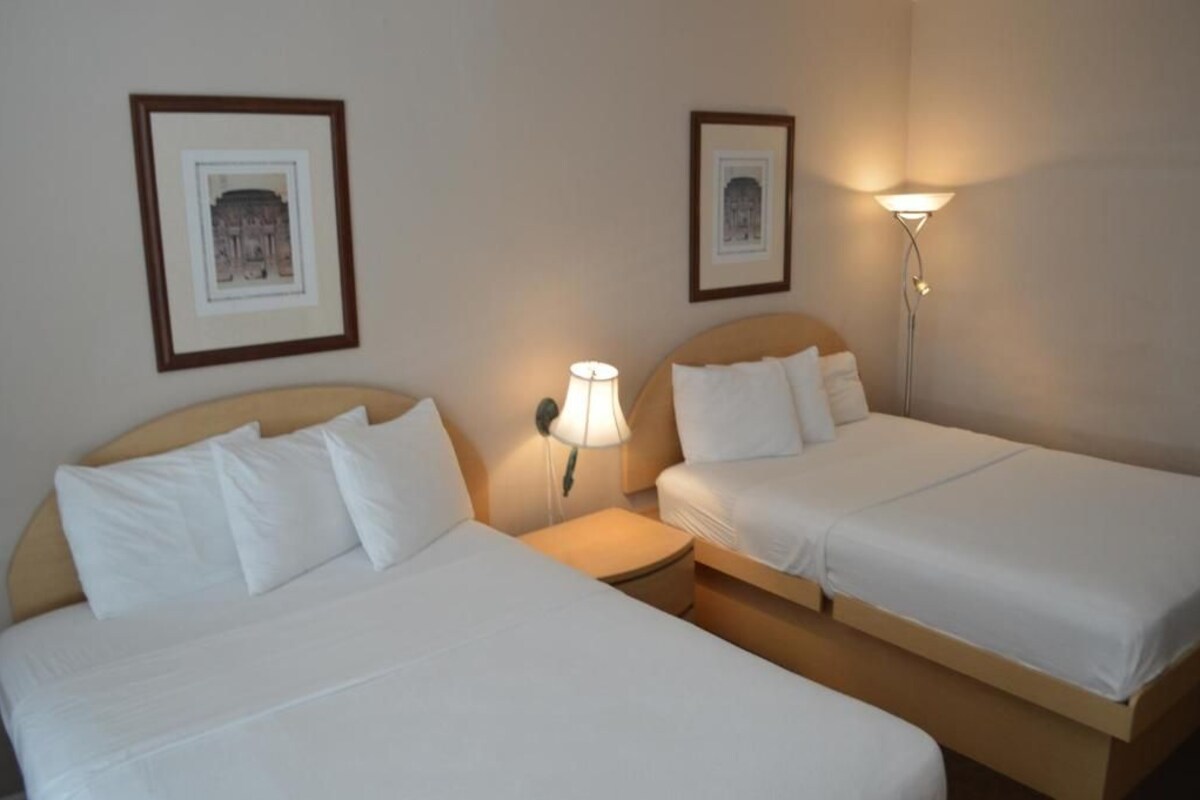 Two single beds with white linens, a nightstand with a lamp, and framed pictures on the wall.