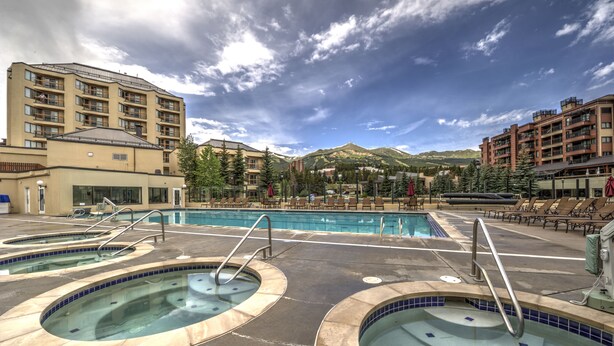 A pool area with multiple hot tubs and lounge chairs, surrounded by buildings and mountains. - Main Street Junction (Breckenridge)