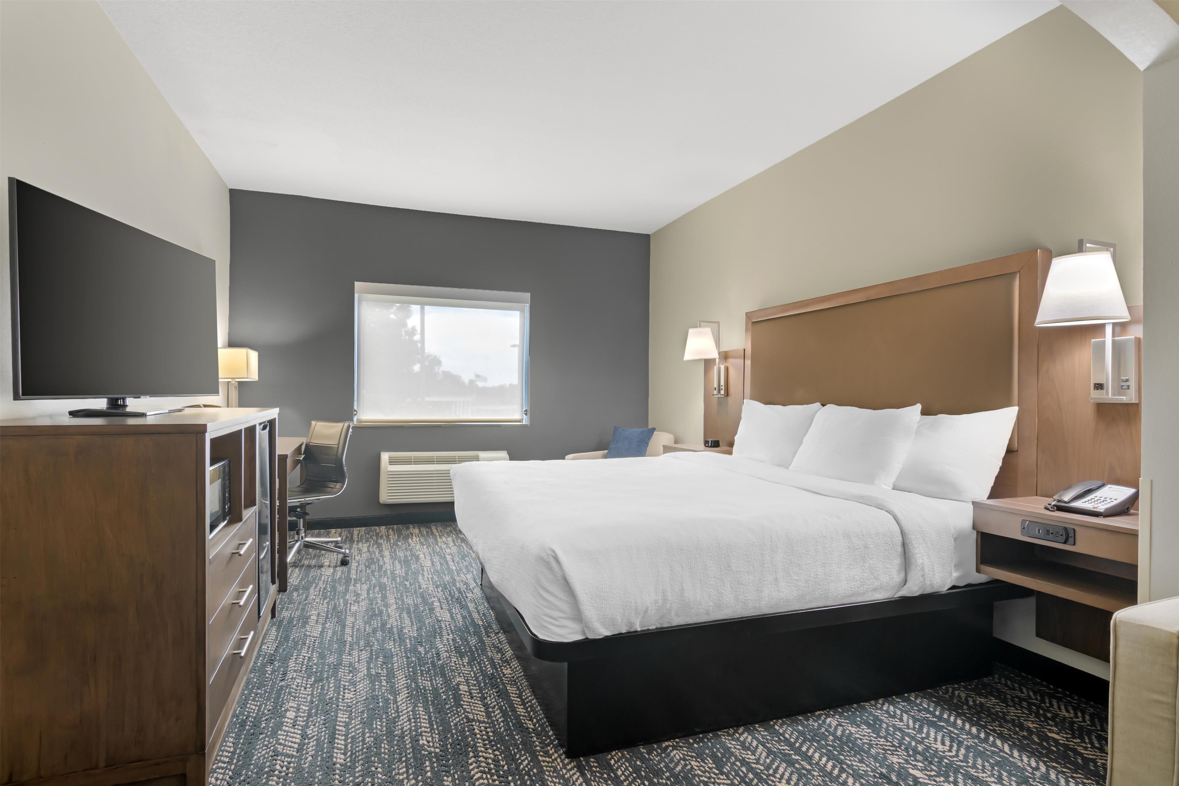 A hotel room with a large bed, bedside lamps, a desk with a lamp, a dresser, and a window with a view.