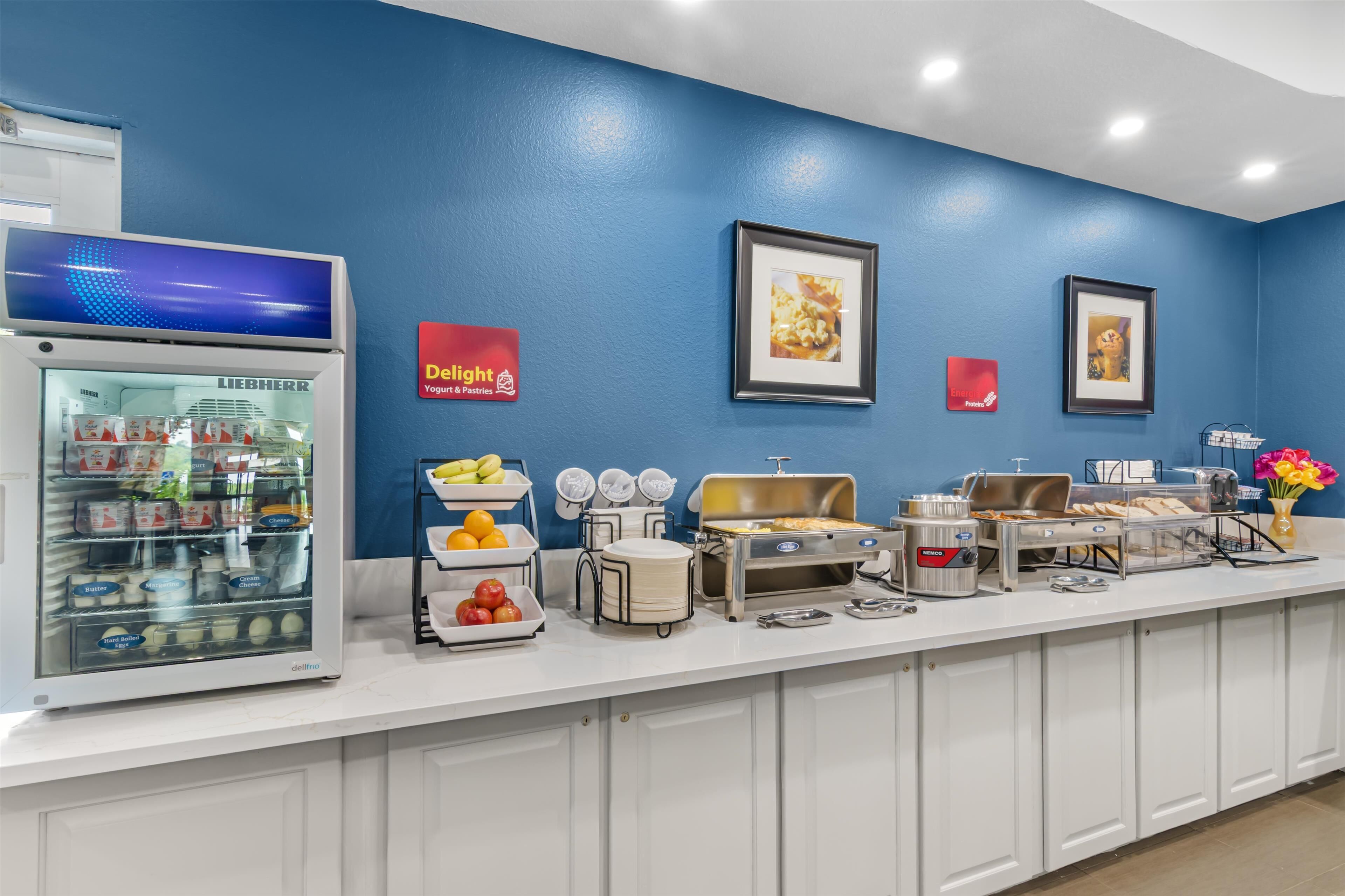 Un bufé de desayuno con diversas opciones de comida, un refrigerador y cuadros en la pared.