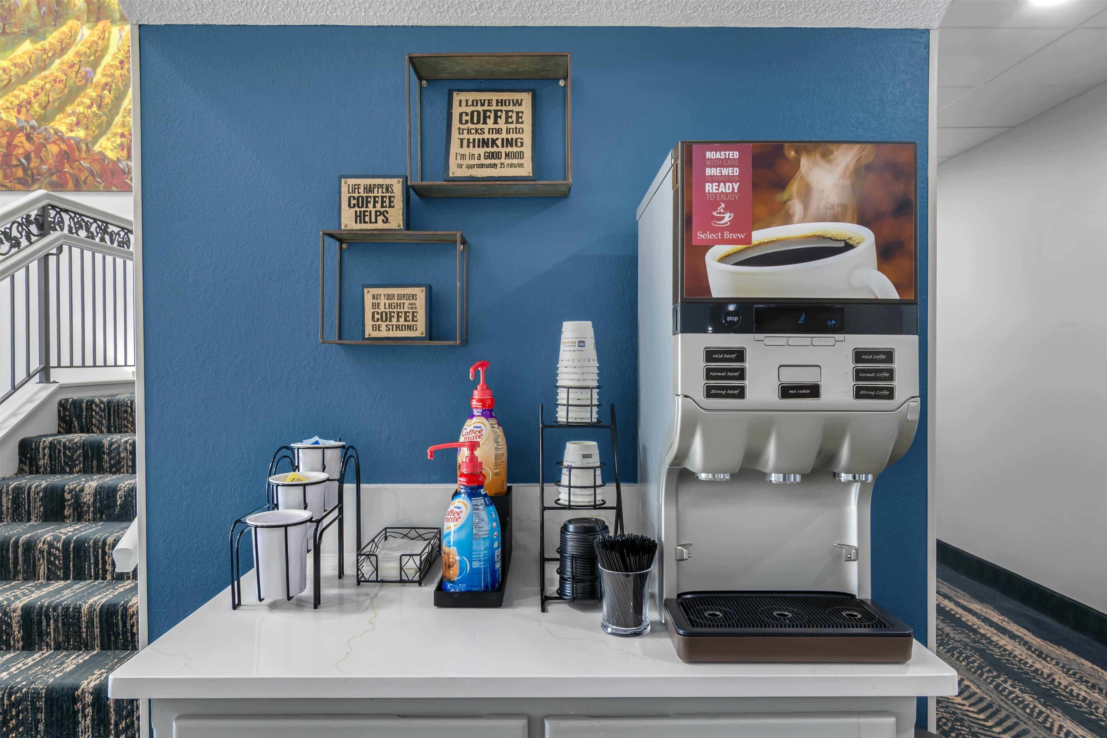 Una estación de café con una máquina de café, tazas y una botella de crema para café.