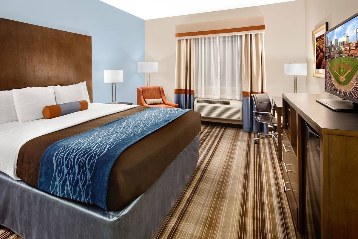A hotel room with a bed, a desk, a chair, a television, and a window with curtains.