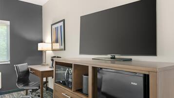 A hotel room with a desk, chair, television, and a Haier refrigerator.