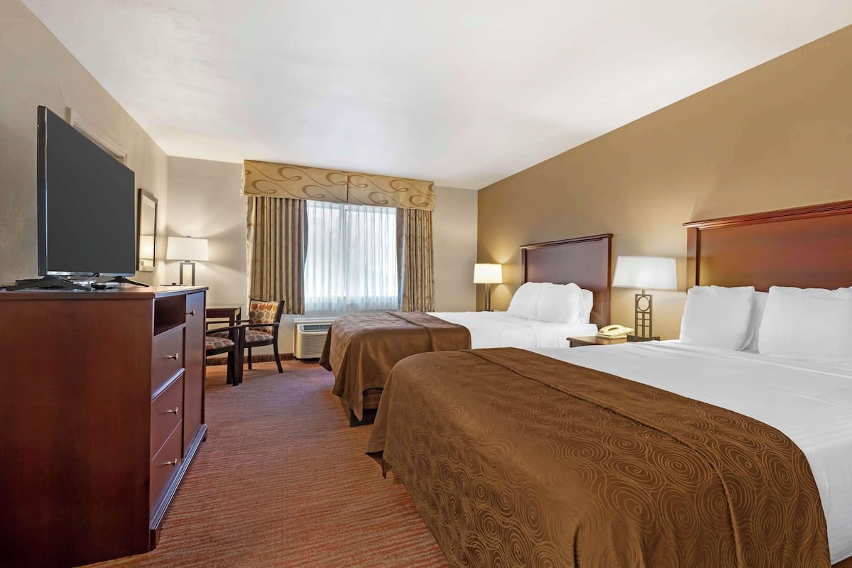A hotel room with two beds, a desk with a chair, a television, and a desk lamp.