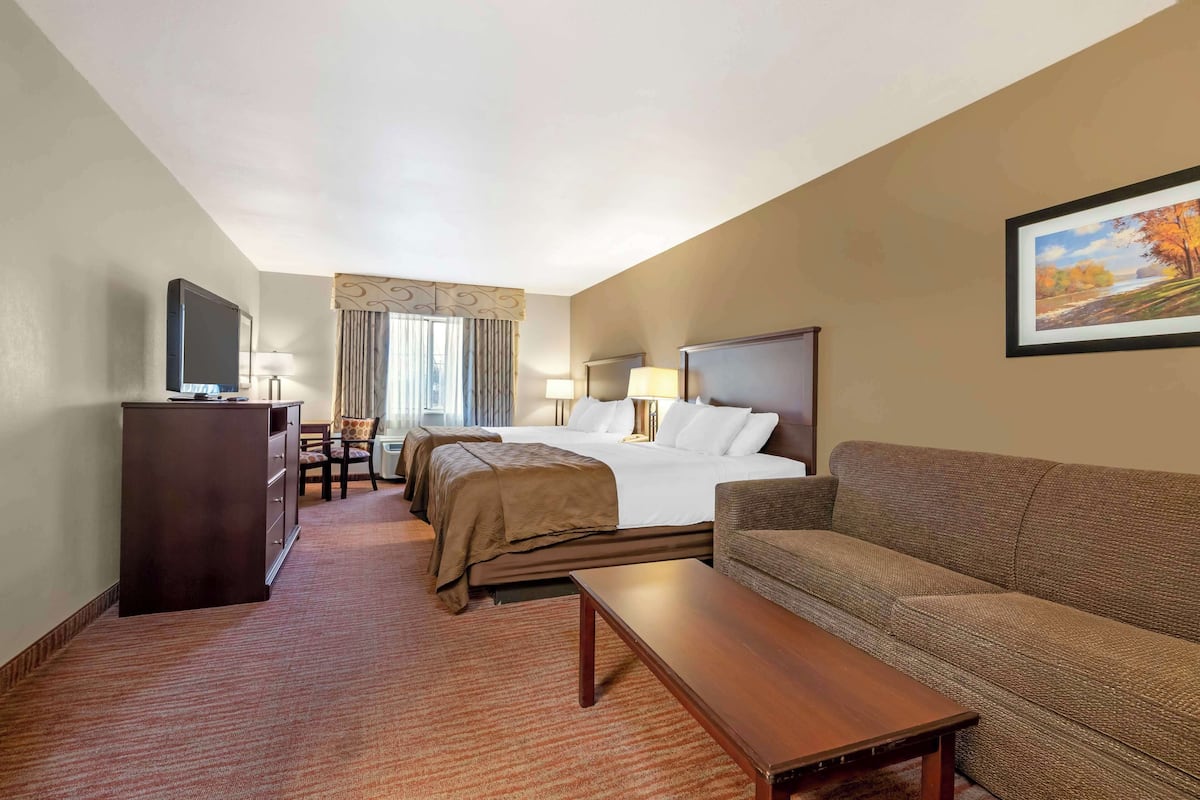 A hotel room with a bed, a sofa, a desk, a TV, and a painting on the wall.