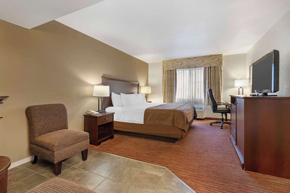 A hotel room with a large bed, a chair, a desk with a TV, and a window with curtains.