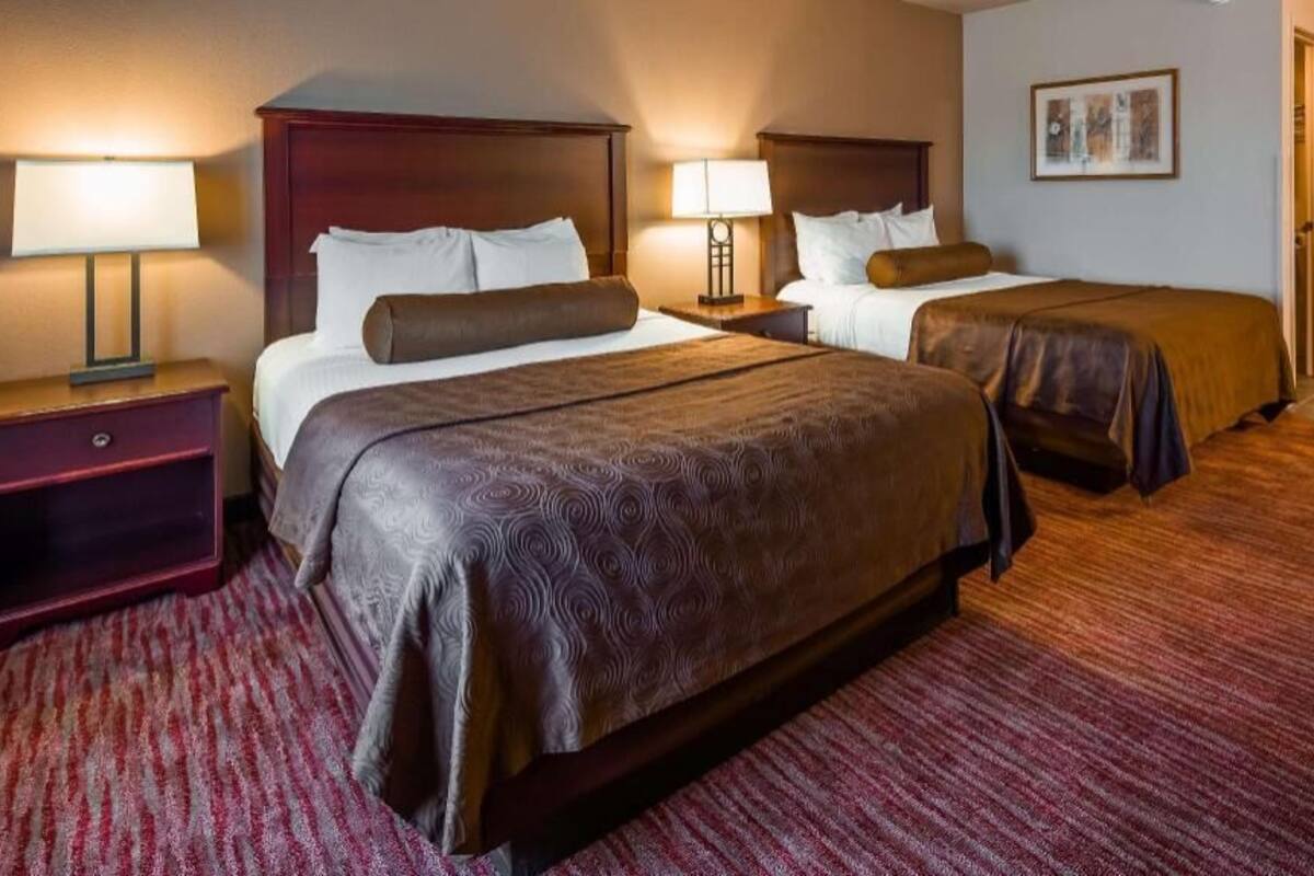 A hotel room with two beds, a red carpet, and a wooden headboard.