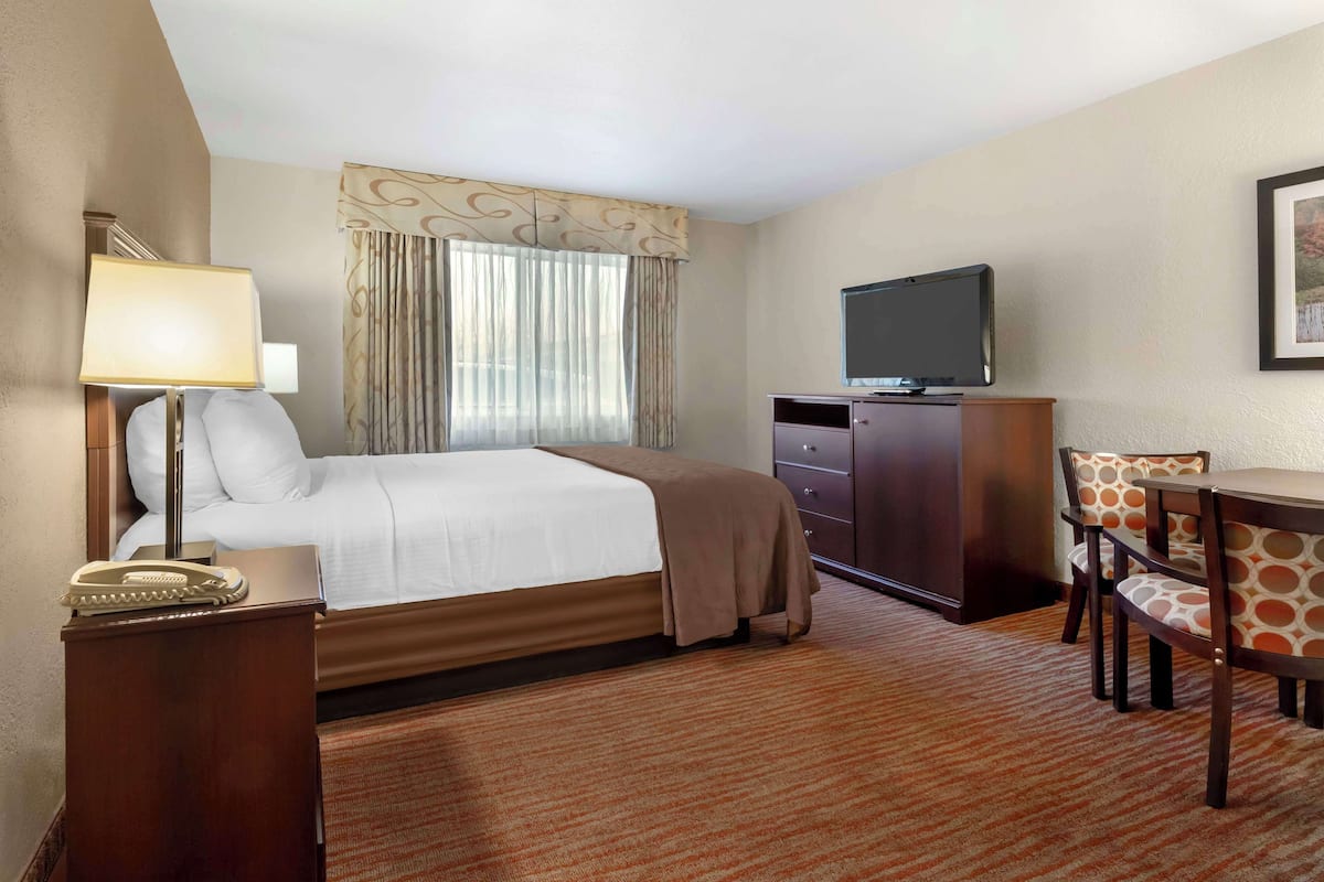 A hotel room with a bed, a desk with a chair, a television, a telephone, and a window with curtains.