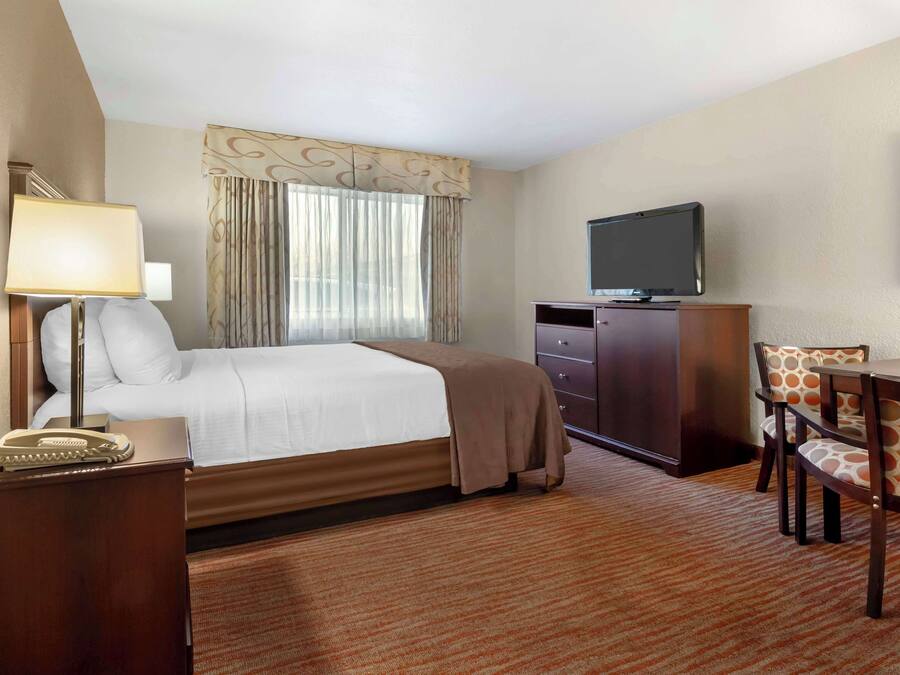 A hotel room with a bed, a desk with a chair, a television, a telephone, and a window with curtains.