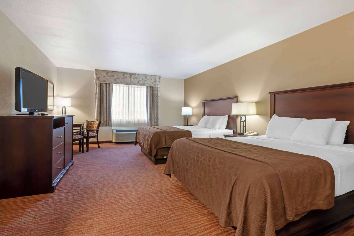 A hotel room with two beds, a desk, a television, and a chair.