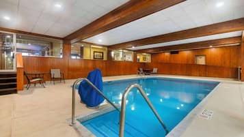 An indoor swimming pool with wooden paneling, a blue pool, and a metal ladder.
