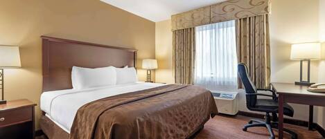 A hotel room with a large bed, a desk with a chair, a lamp, and a heater.