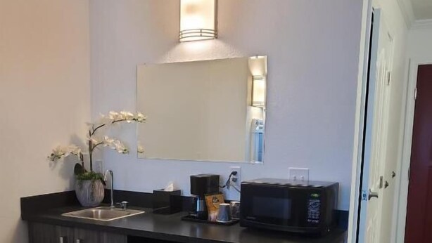 A compact kitchenette with a microwave, sink, and dark cabinets. - Signature Hotel by Tachi (Hanford)