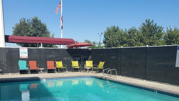 A clear swimming pool with a flag, a poolside area with chairs, and a fence.