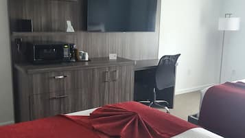 A hotel room with a bed, a desk with a flat-screen TV, a microwave, and a small plant.