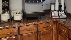 A self-service beverage station with a touchscreen menu, a coffee machine, and a dish rack with cups and plates.