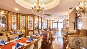 Un vaste espace dédié à la salle à manger, avec de nombreuses tables, des lustres décoratifs et des chaises en bois d’époque.