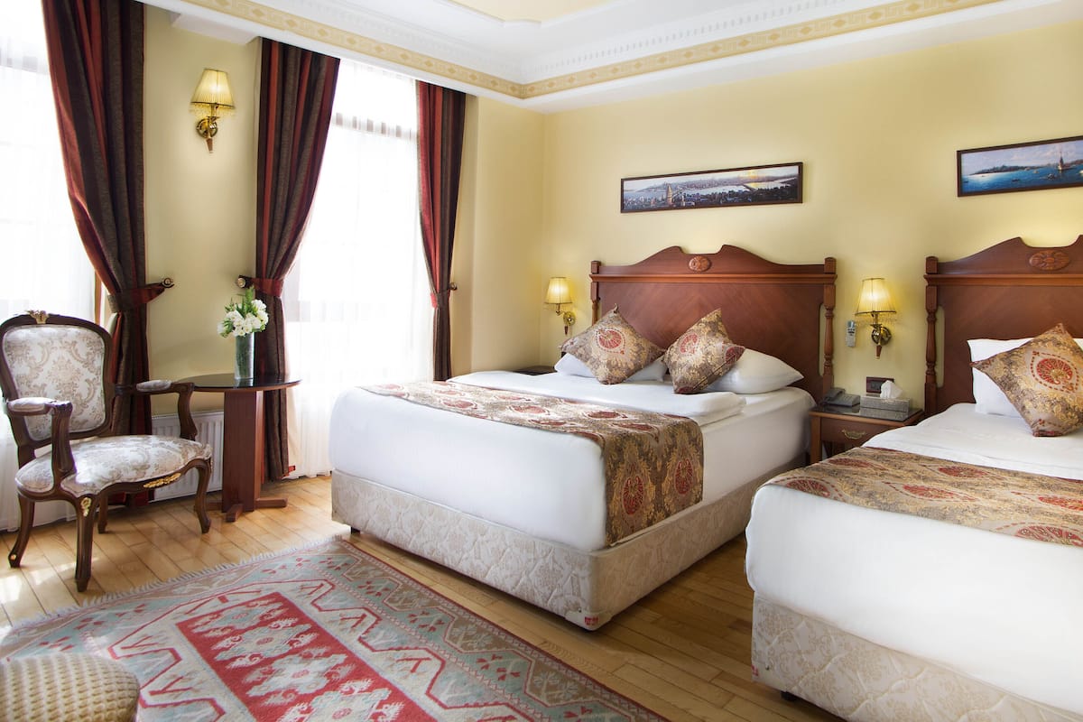 Een hotelkamer met twee bedden, een zithoek met een stoel, een kleine tafel en een decoratief vloerkleed.