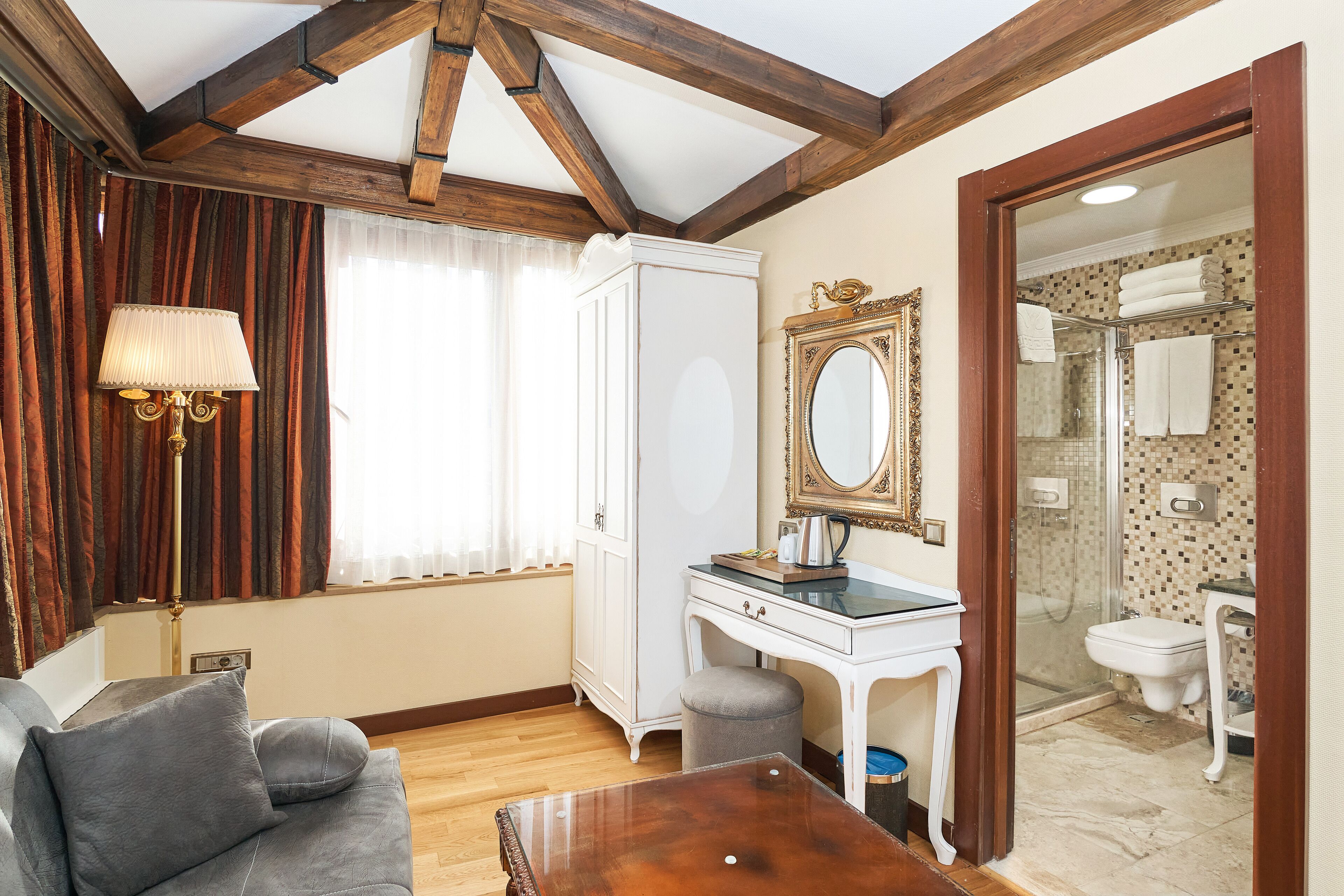 Una habitación con sofá, escritorio, armario y baño visible a través de una puerta abierta.