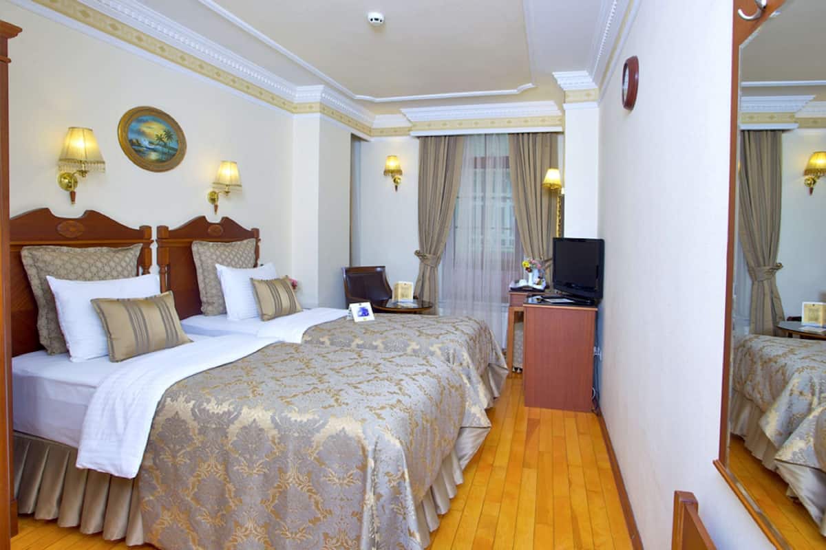 Een hotelkamer met twee bedden, een bureau met een televisie en wandlampen.