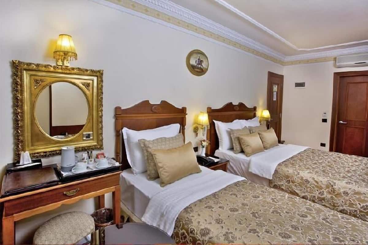 Een hotelkamer met twee bedden, een houten dressoir, een spiegel en een wandklok.