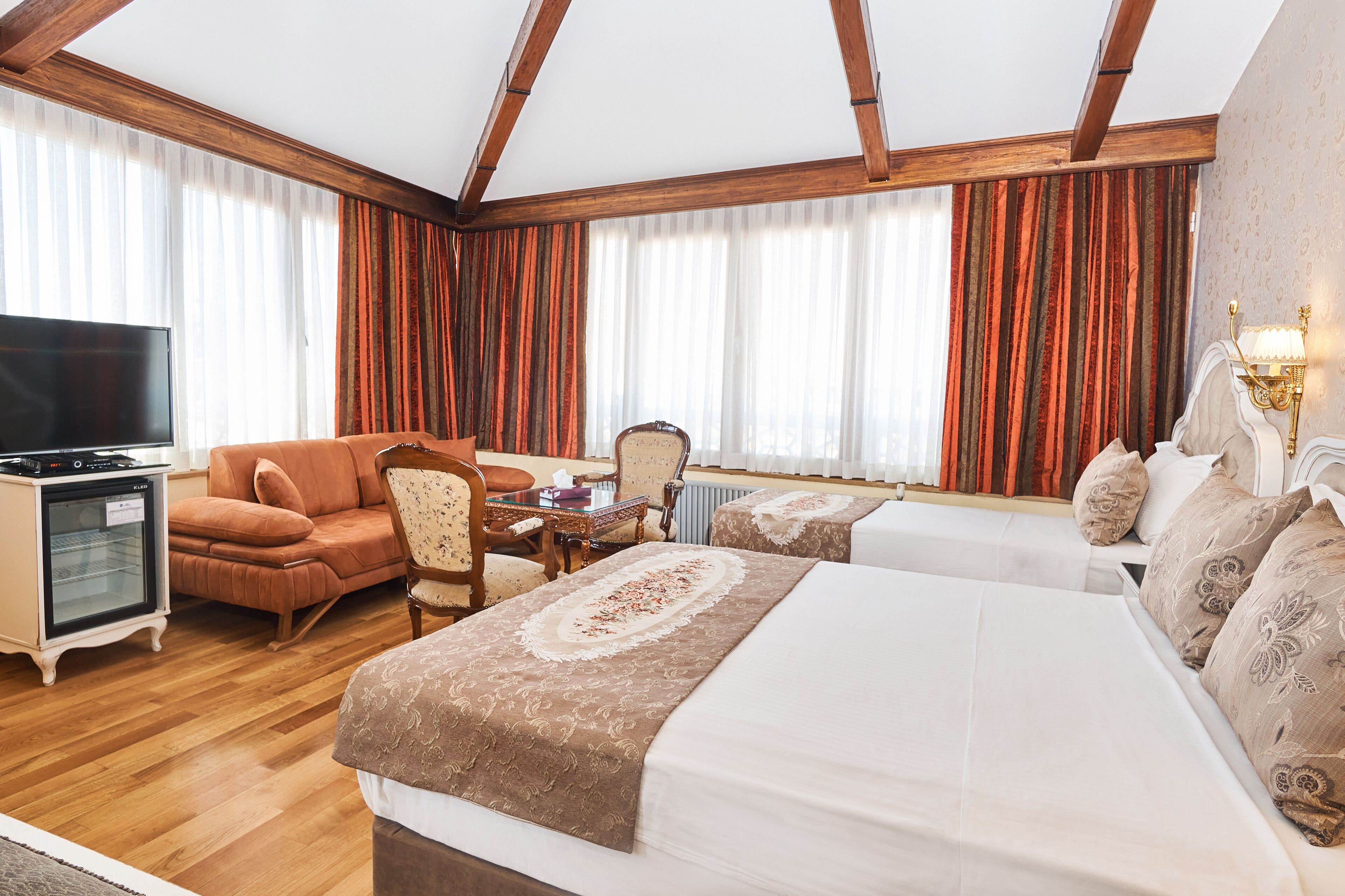 A hotel room with a large bed, a sofa, a TV, and a dining table.