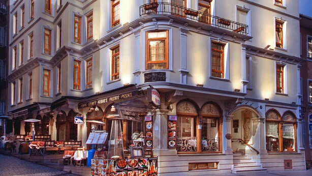 Un hôtel à plusieurs étages, de style architectural classique, doté de balcons et d’un restaurant situé au rez-de-chaussée.
