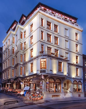 Un hotel de varios pisos con un estilo arquitectónico clásico, que cuenta con balcones y un restaurante a nivel de calle.