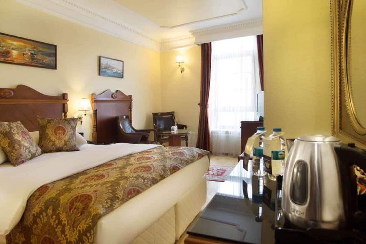 Een hotelkamer met een groot bed, een bureau met een waterkoker en een stoel.