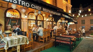 Un espace de restauration en plein air, aménagé par un chef de bistrot, avec des tables et des bancs en bois, et un sol recouvert d’une moquette verte.