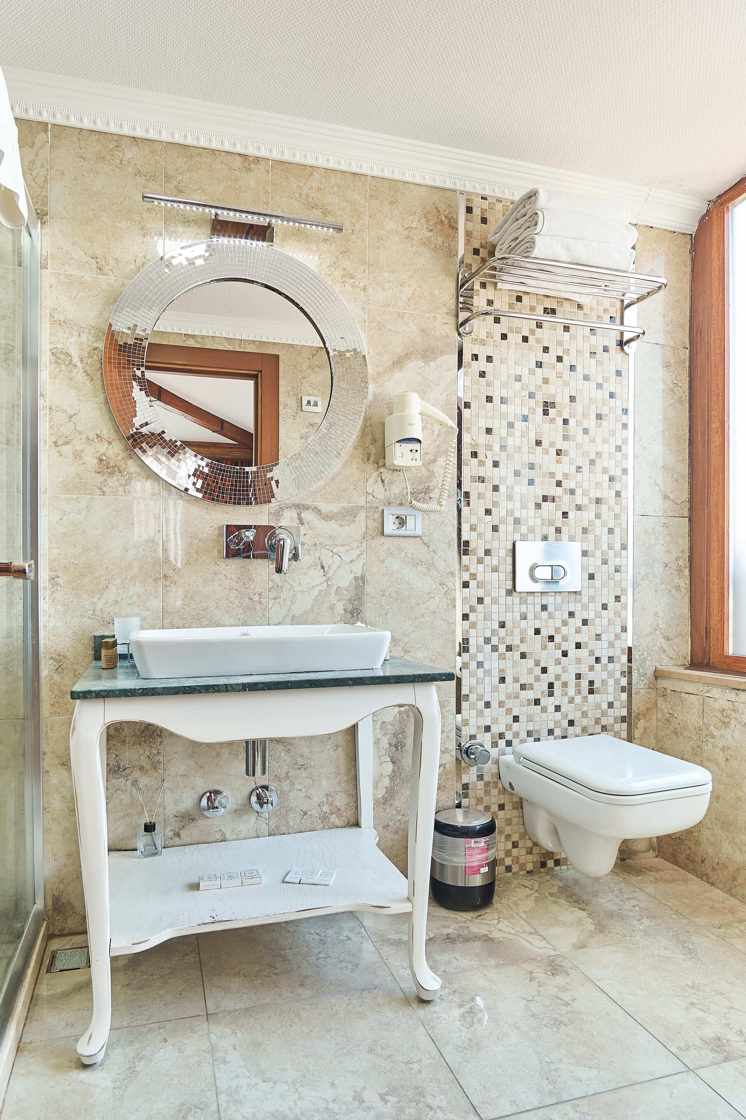 A bathroom with a round mirror, a sink, a toilet, and a shower area.