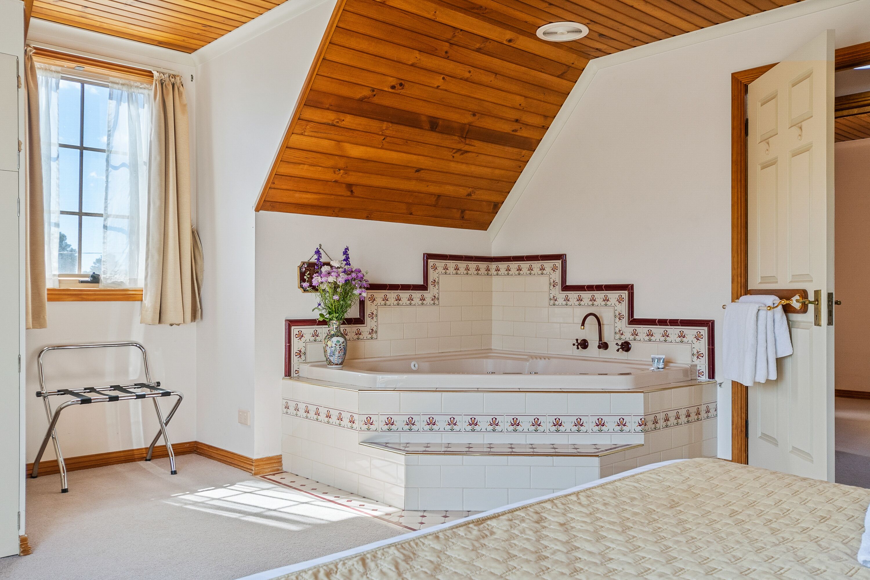 Un dormitorio con una cama grande, techo de madera, baño con bañera y ventana con cortinas.