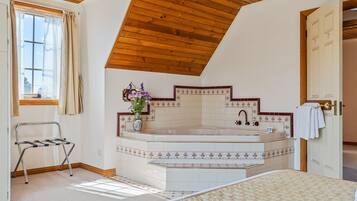 Un dormitorio con una cama grande, techo de madera, baño con bañera y ventana con cortinas.
