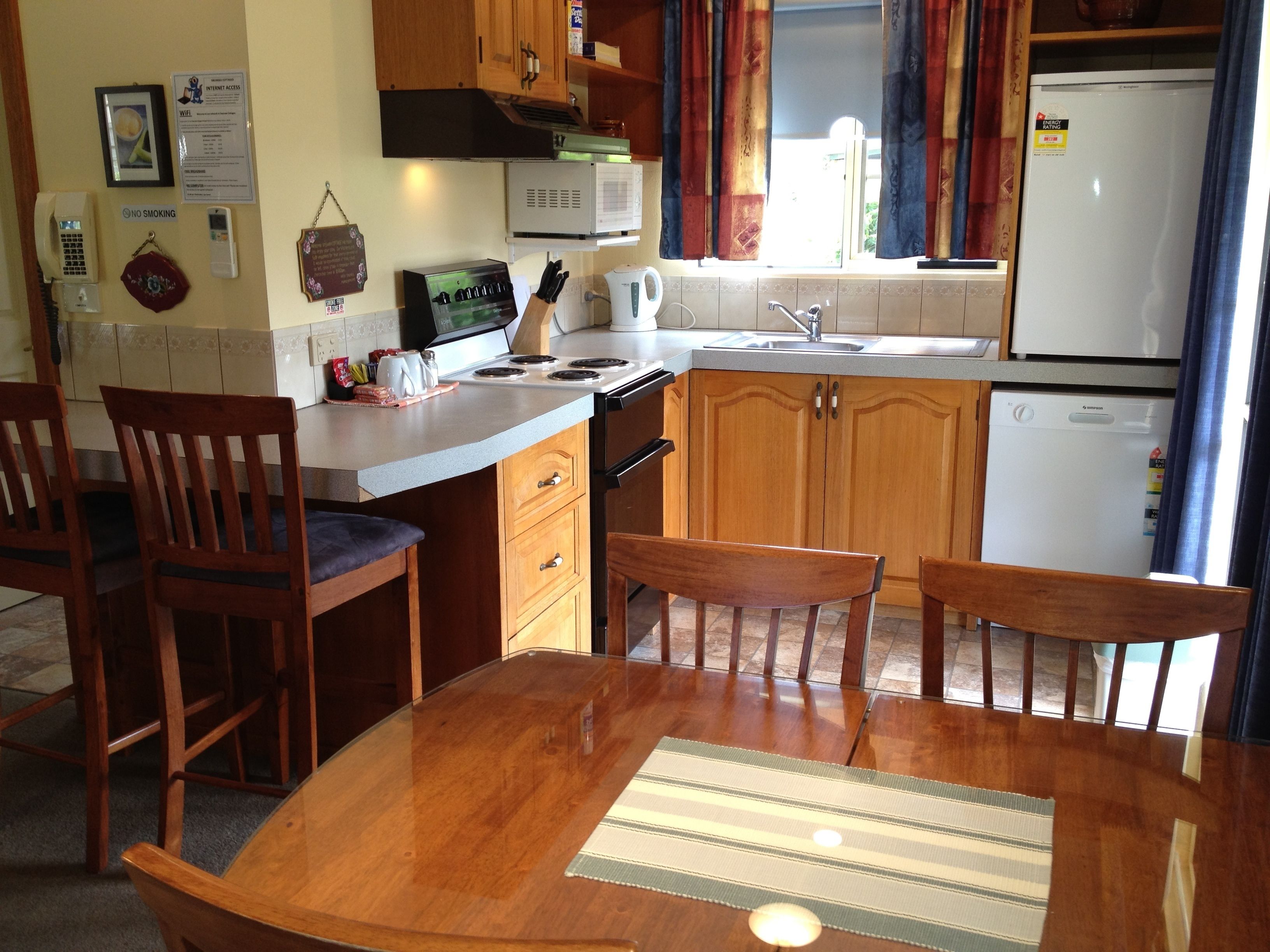 Une cuisine compacte avec des meubles en bois, un four à micro-ondes, une cuisinière et un réfrigérateur. On y trouve une table à manger avec des chaises et un petit tapis.