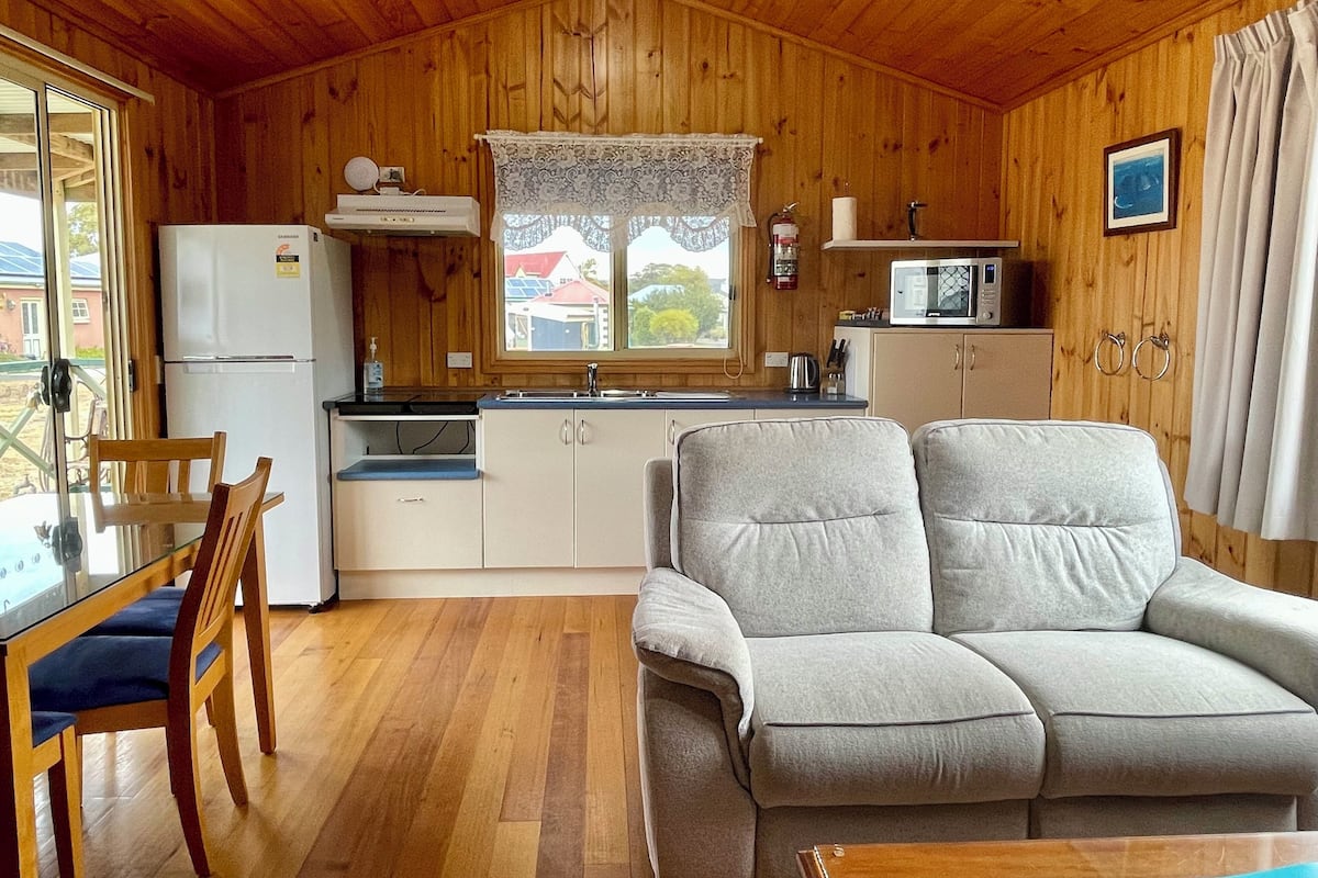 Cocina acogedora de estilo rústico con paredes de madera, una mesa de comedor con sillas, un sofá y un refrigerador.