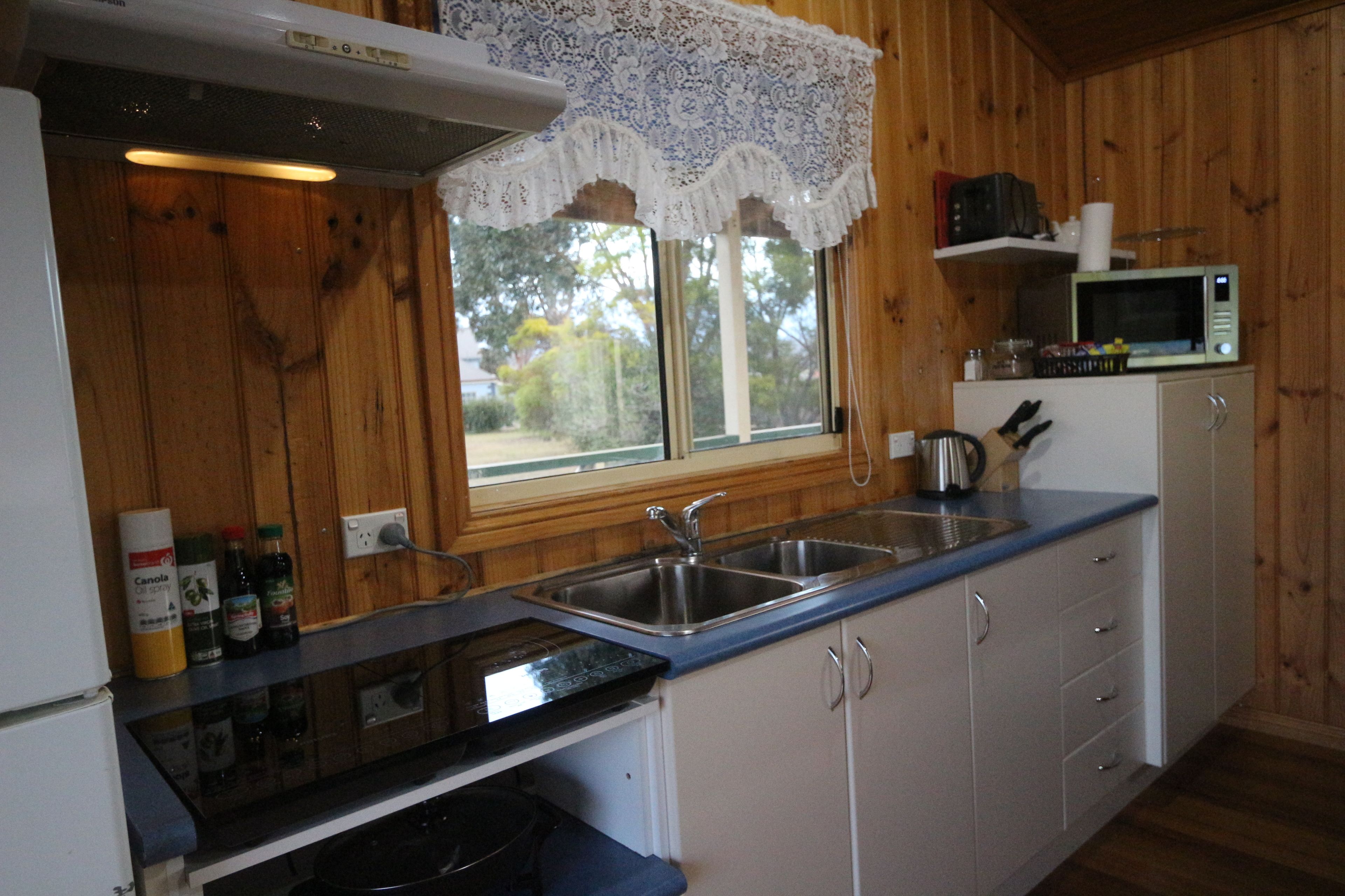 Une cuisine avec des murs en bois, une fenêtre ornée de rideaux en dentelle, un four à micro-ondes et un évier.