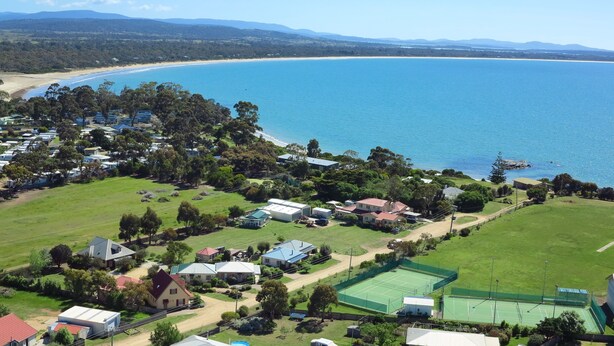 Vista aerea di una zona residenziale costiera con case, un campo da tennis e una spiaggia.