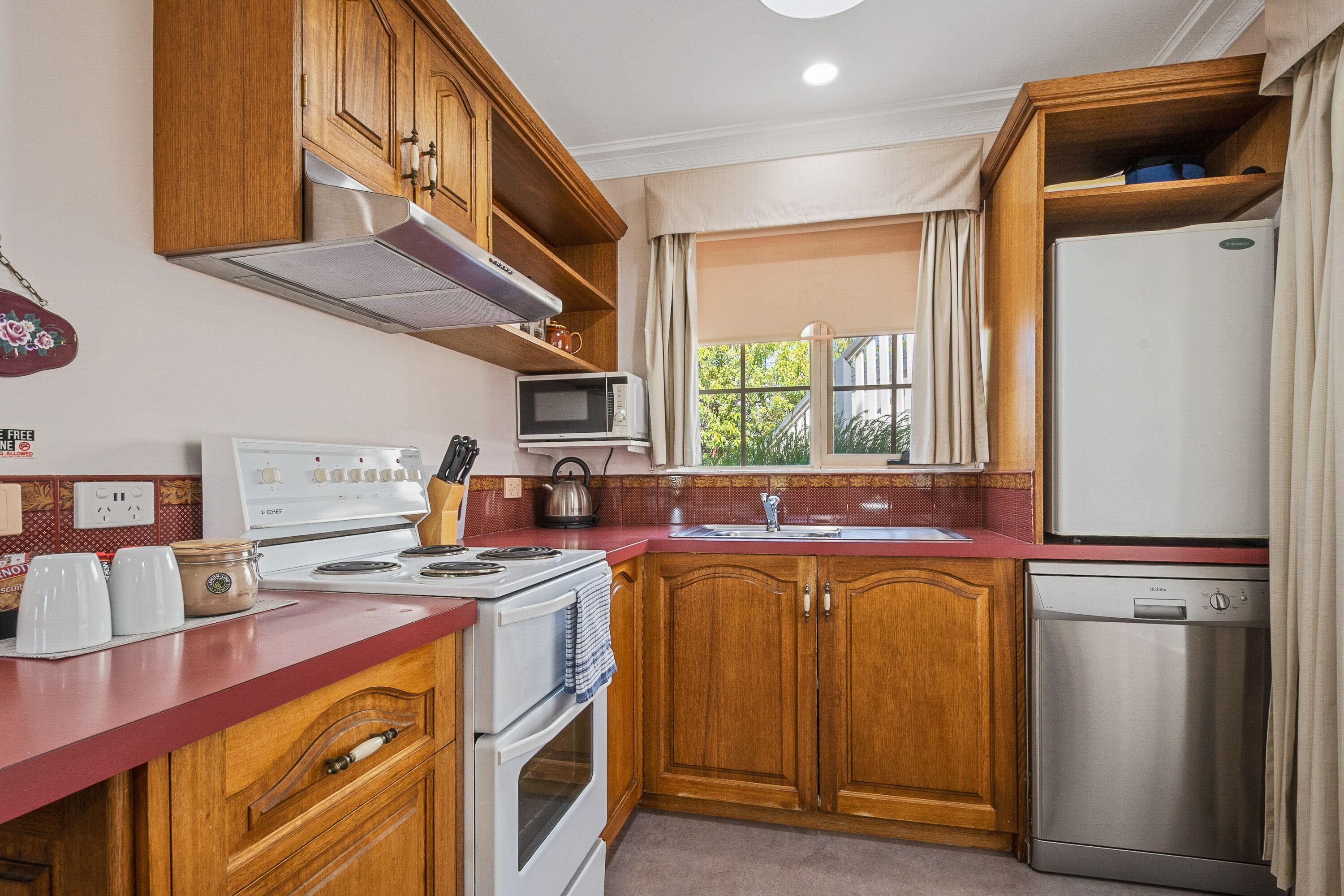 Una cocina con gabinetes de madera, microondas, estufa, fregadero y lavavajillas.