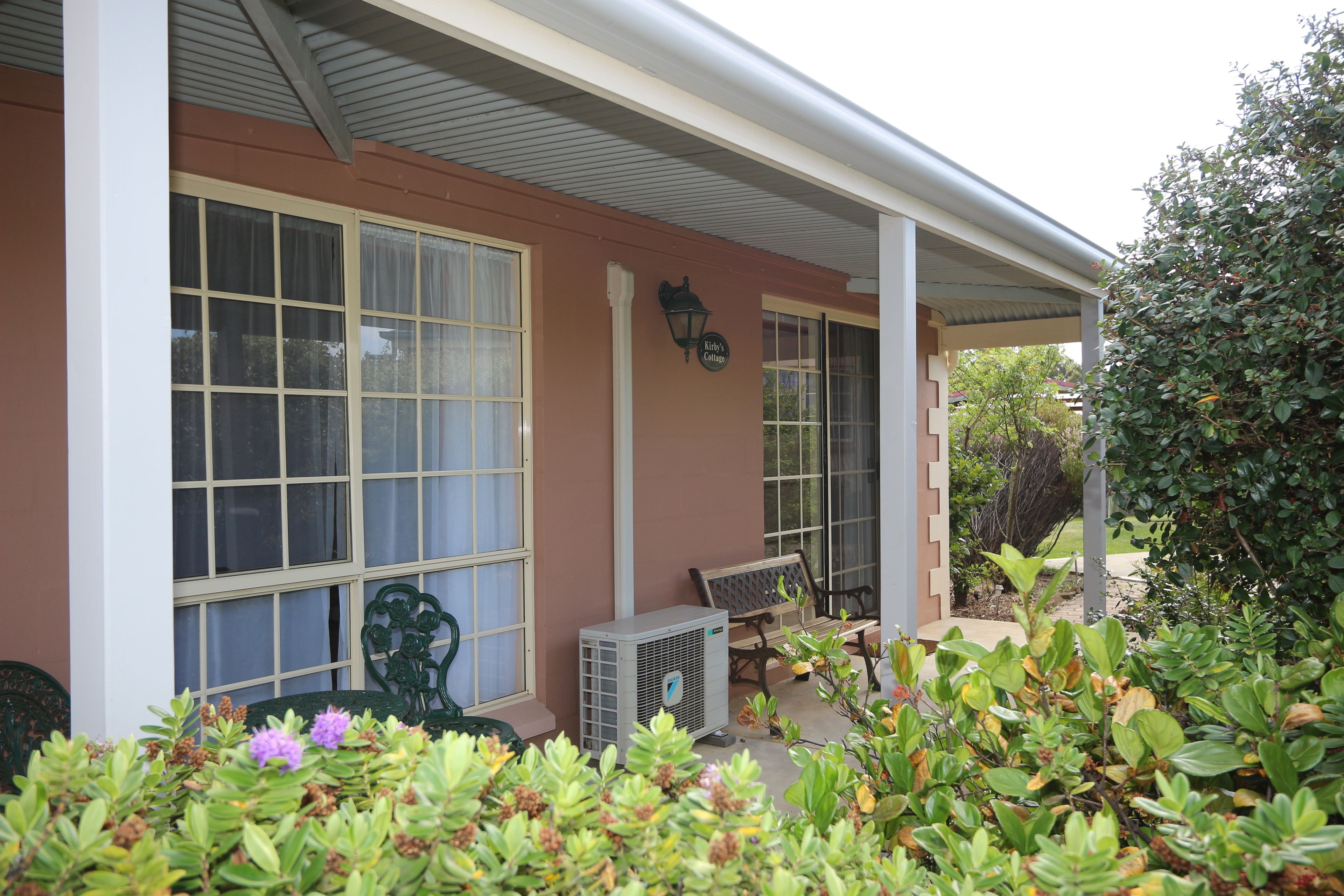 A house with a porch, large windows, a bench, and a small garden area.