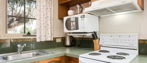 A kitchen with wooden cabinets, a white stove, a microwave, and a window with curtains.