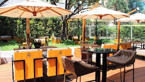 An outdoor dining area with wooden furniture, large umbrellas, and a view of the garden. - Grand Mercure Sao Paulo Vila Olimpia (São Paulo)