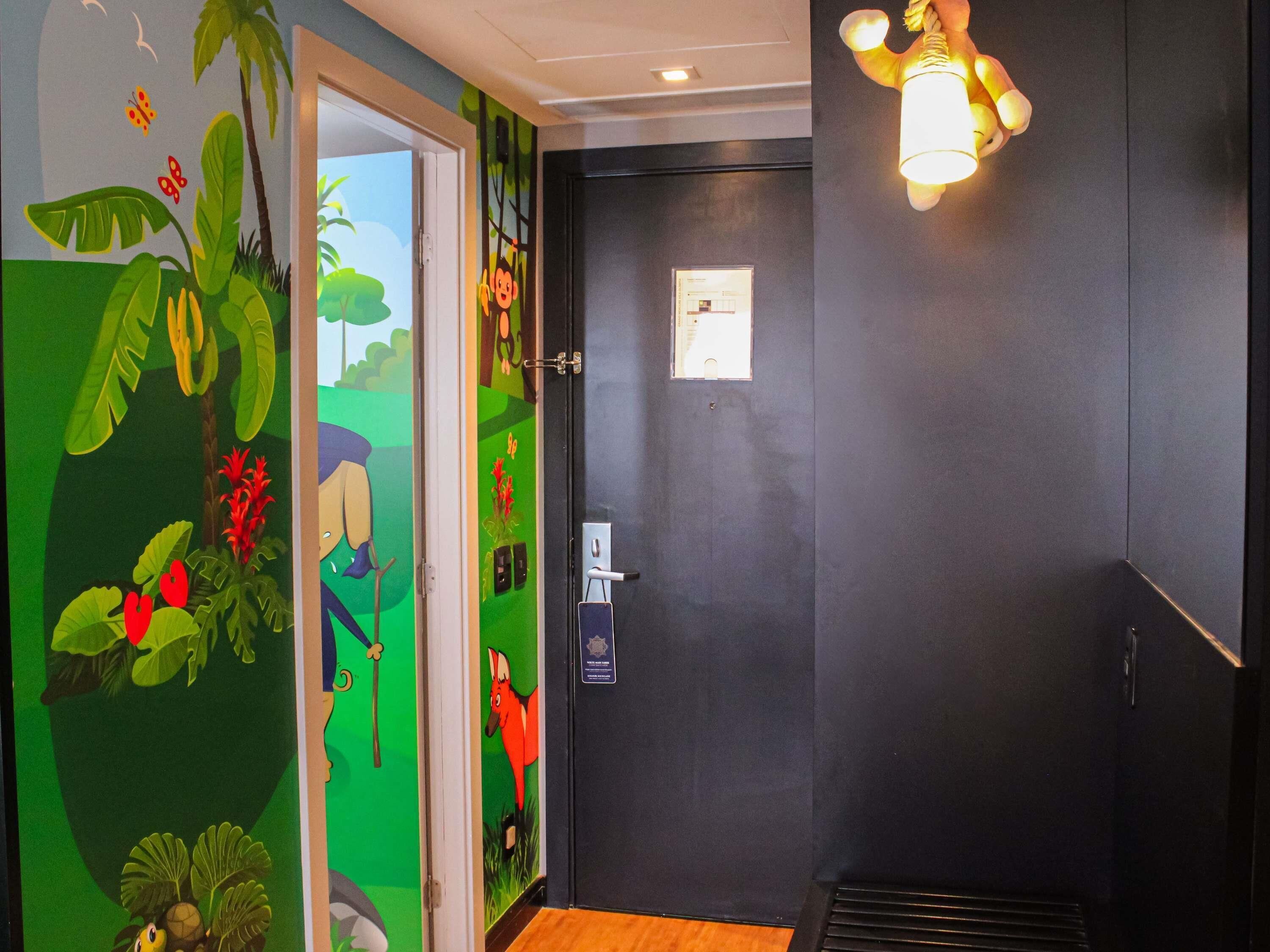 Una habitación con una puerta, una pared con un mural, una lámpara y una ventana.
