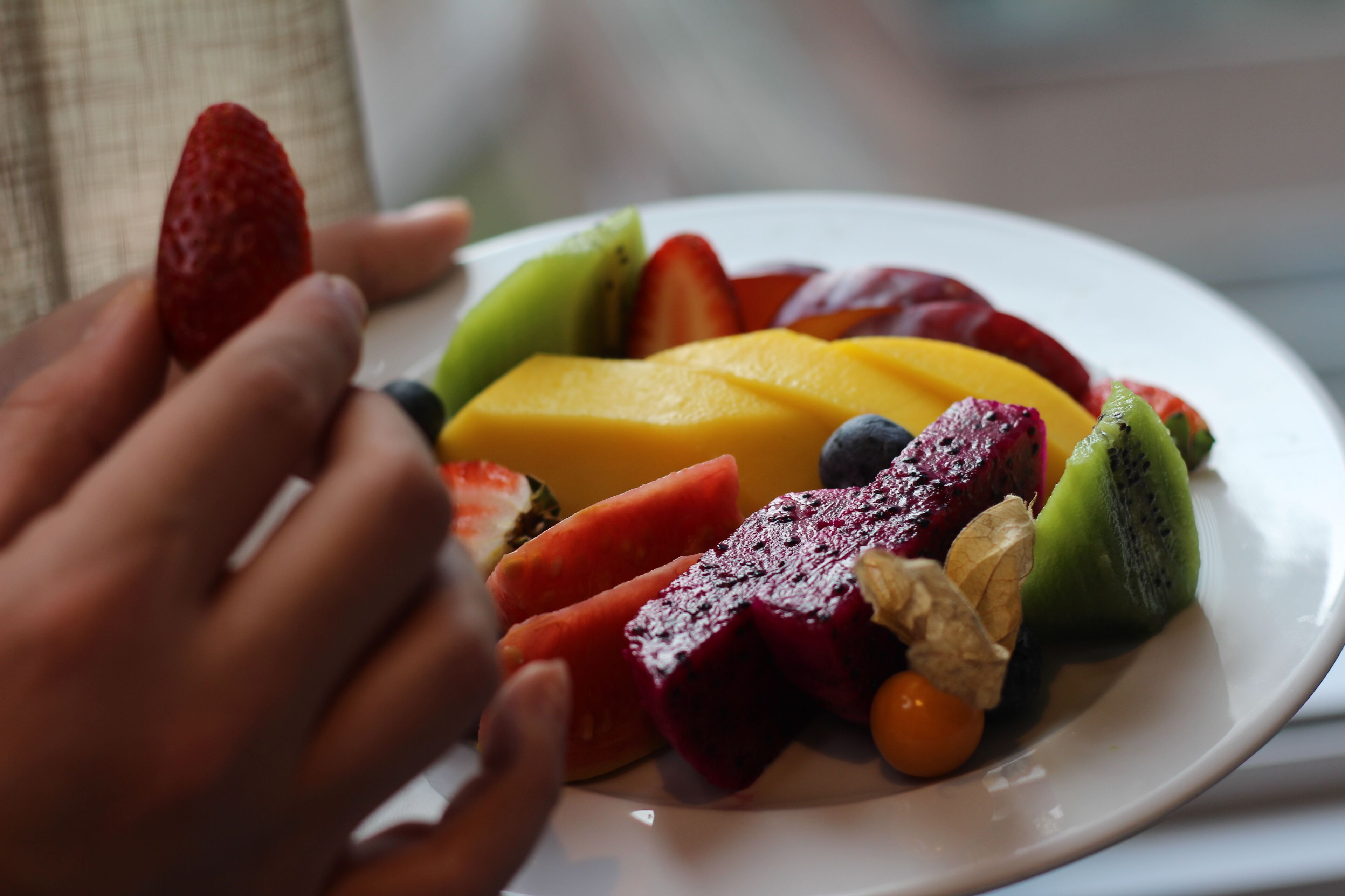 A plate of assorted fruits including strawberries, mango, kiwi, and dragon fruit.