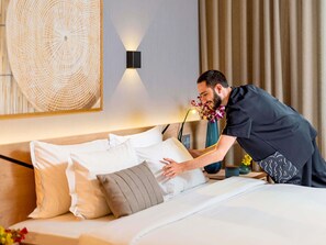 A hotel room with a neatly made bed, a wall-mounted light fixture, and a decorative woven wall art piece.