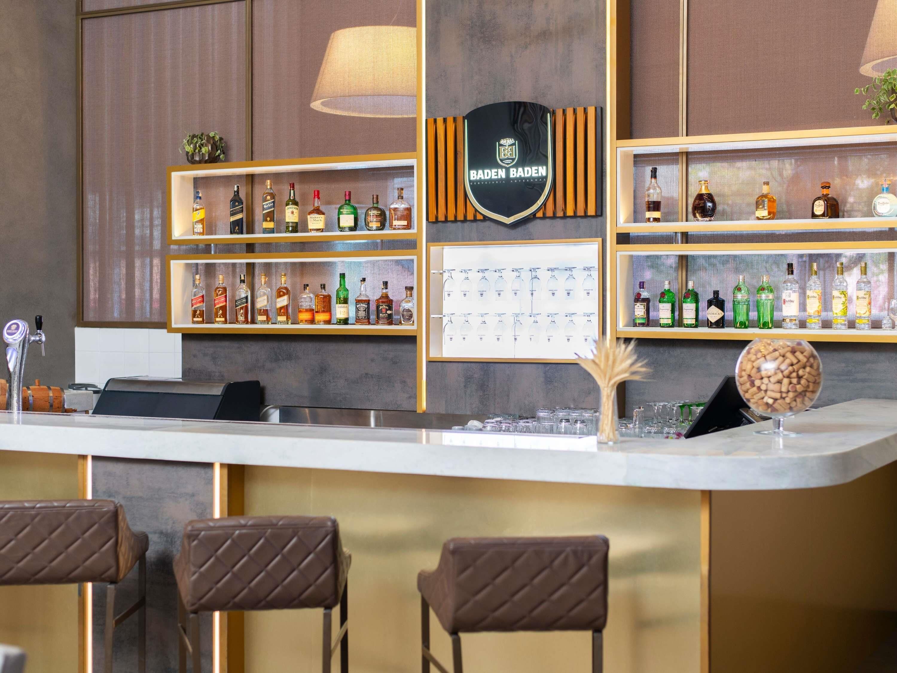 A bar area with shelves of liquor bottles, a logo on the wall, and bar stools.