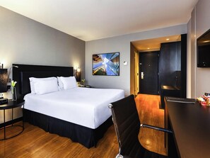A hotel room with a large bed, a desk, a chair, a TV, and a painting on the wall. - Grand Mercure Sao Paulo Vila Olimpia (São Paulo)