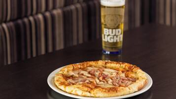 Eine Pizza auf einem Teller, im Hintergrund ein Glas Bier.