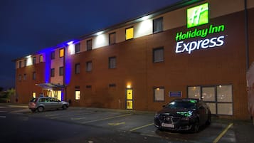 Edificio de Holiday Inn Express con un estacionamiento y dos coches aparcados en la entrada.